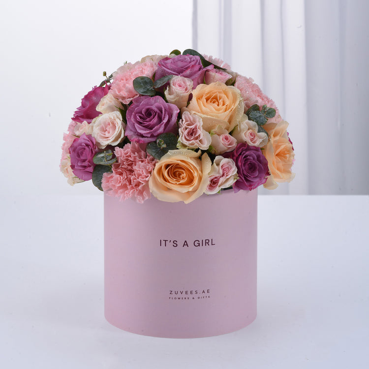 Soft pink box holds lush purple, peach, and blush roses with greenery, celebrating "It&