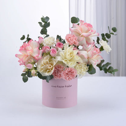 Soft pink and white roses, carnations, eucalyptus in pastel pink cylinder with Arabic birthday message.
