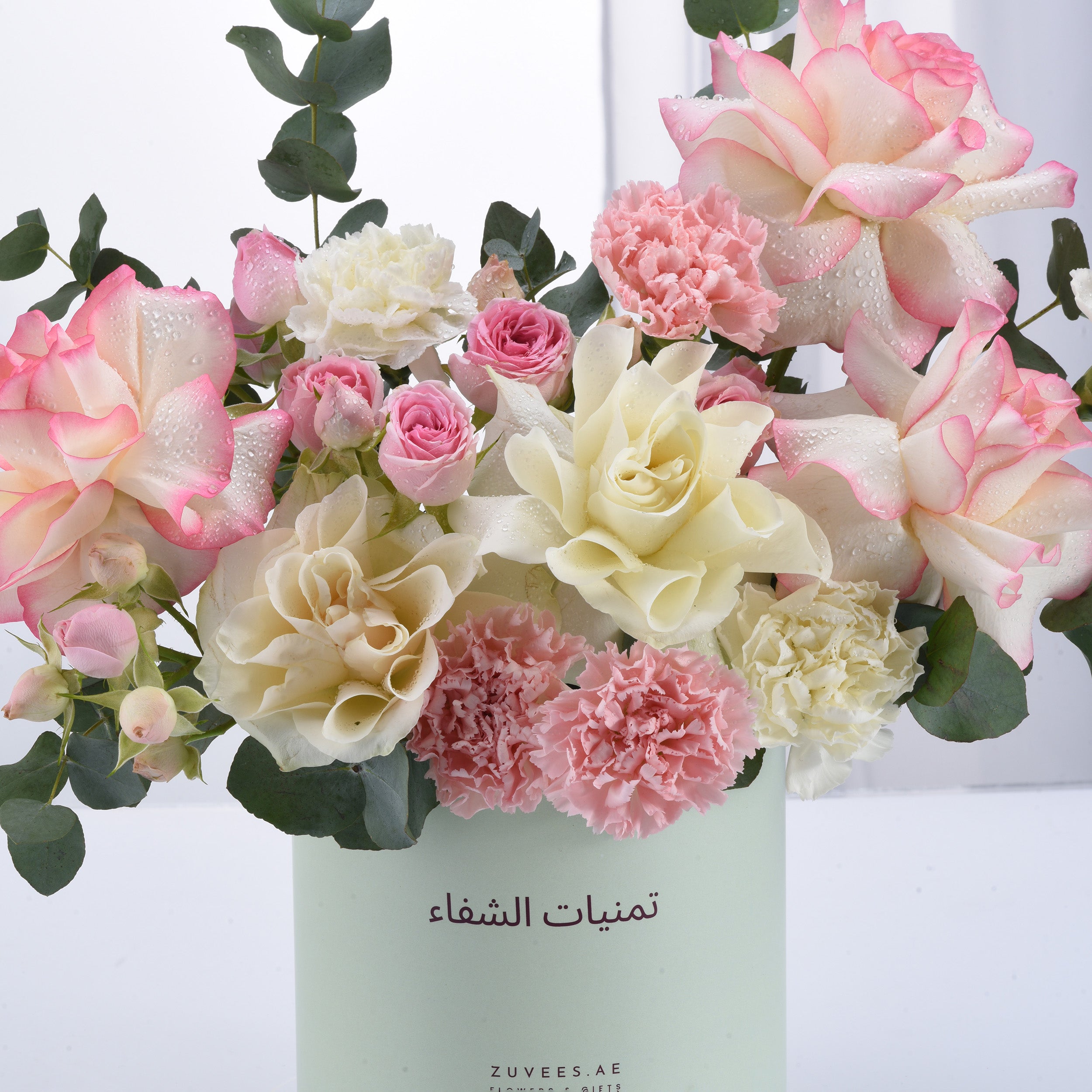 Pastel pink and cream roses, carnations, and eucalyptus in mint vase.