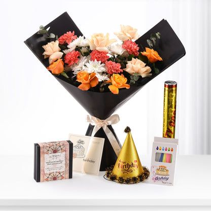 Vibrant orange, peach, and white flowers in black wrap, paired with golden birthday hat, candles, and caramel gift box.