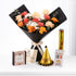 Vibrant orange, peach, and white flowers in black wrap, paired with golden birthday hat, candles, and caramel gift box.