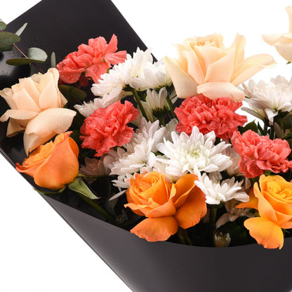 Vibrant orange, peach, and coral roses and carnations with dewdrops, elegantly wrapped in glossy black paper.