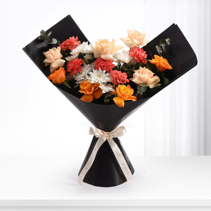 Vibrant orange, peach, coral, and white blooms elegantly wrapped in sleek black paper with gold ribbon.