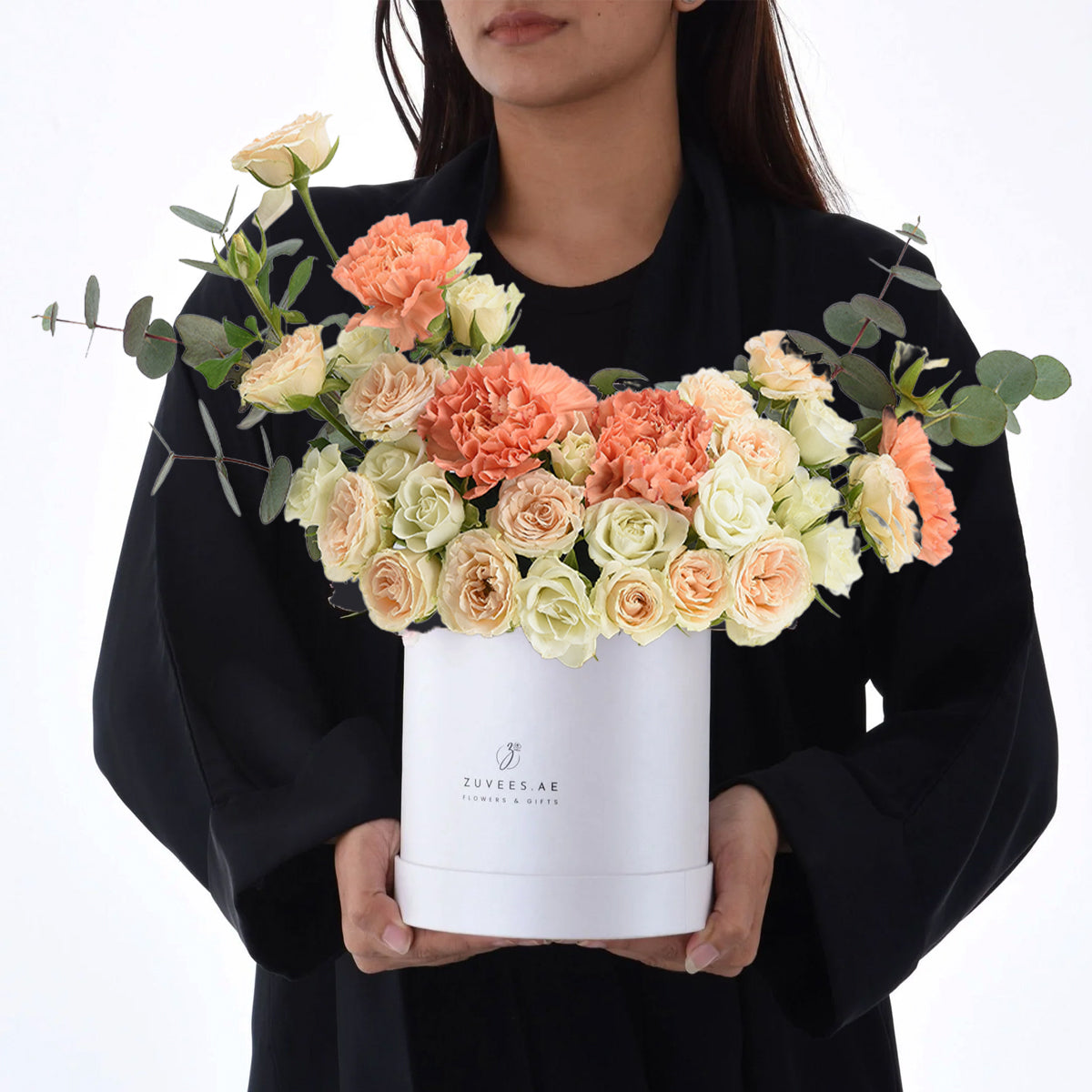 White box holds peach roses and carnations with eucalyptus, elegant gift presentation.