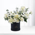 Elegant white roses and eucalyptus in matte black cylindrical gift box.