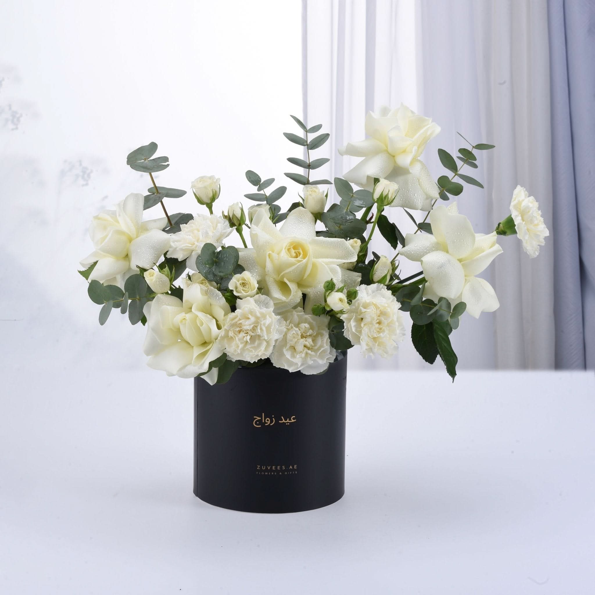 Elegant white roses and carnations in sleek black box with gold text.