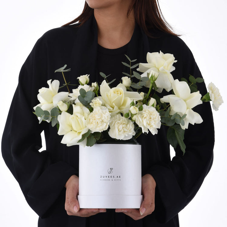 Elegant white roses and carnations in sleek white box held by person.