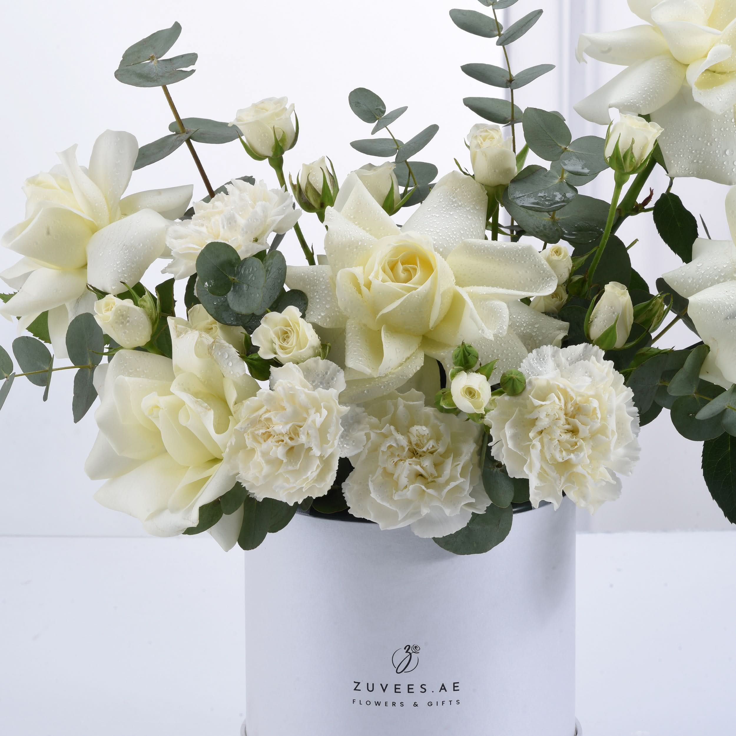 Elegant white roses, carnations, and eucalyptus in a sleek Zuvees box, dew-kissed and fresh.