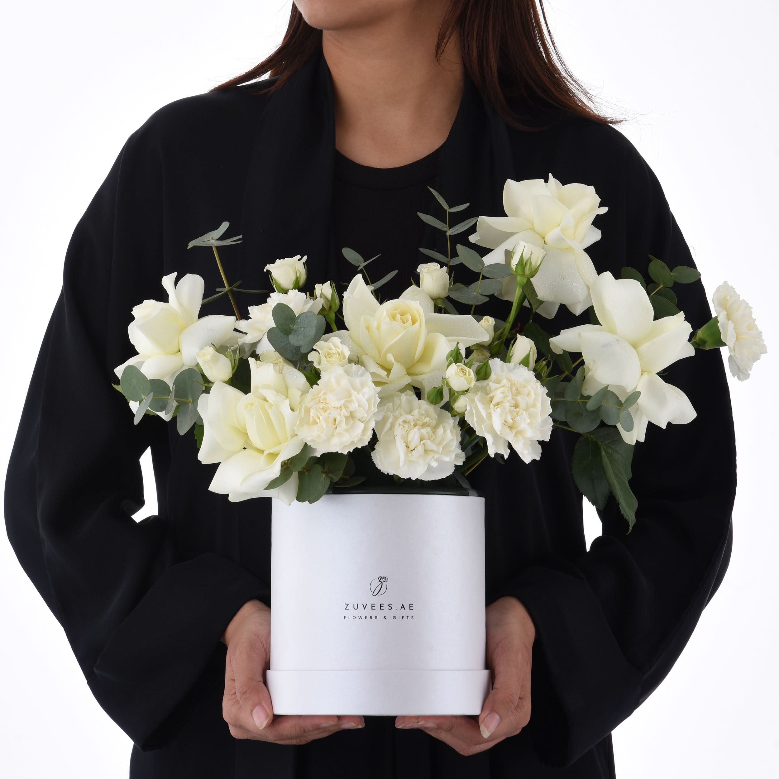 Elegant white roses and carnations in minimalist white box held by person.