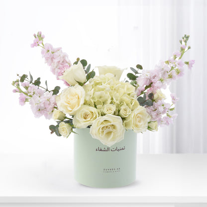 Pastel green cylinder vase holds creamy white roses and soft pink blooms against bright white background.
