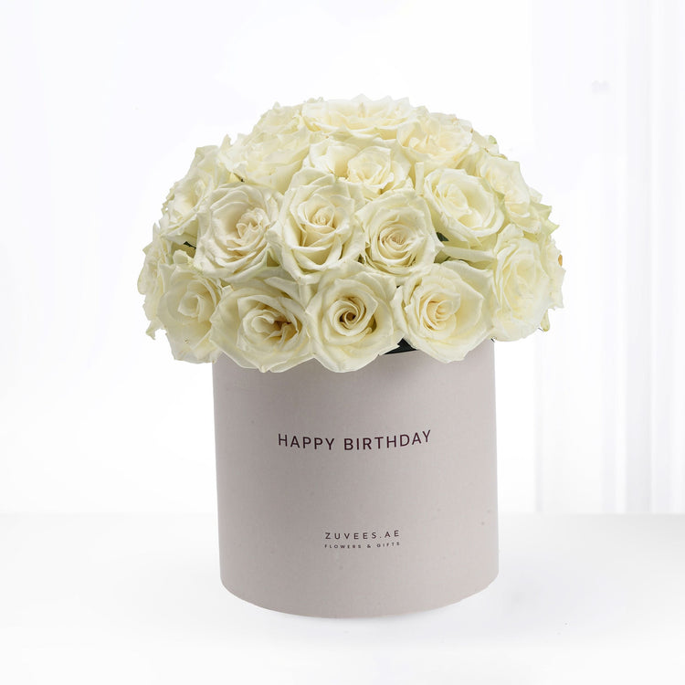 Luxurious cream roses overflowing from a matte taupe birthday hat box.