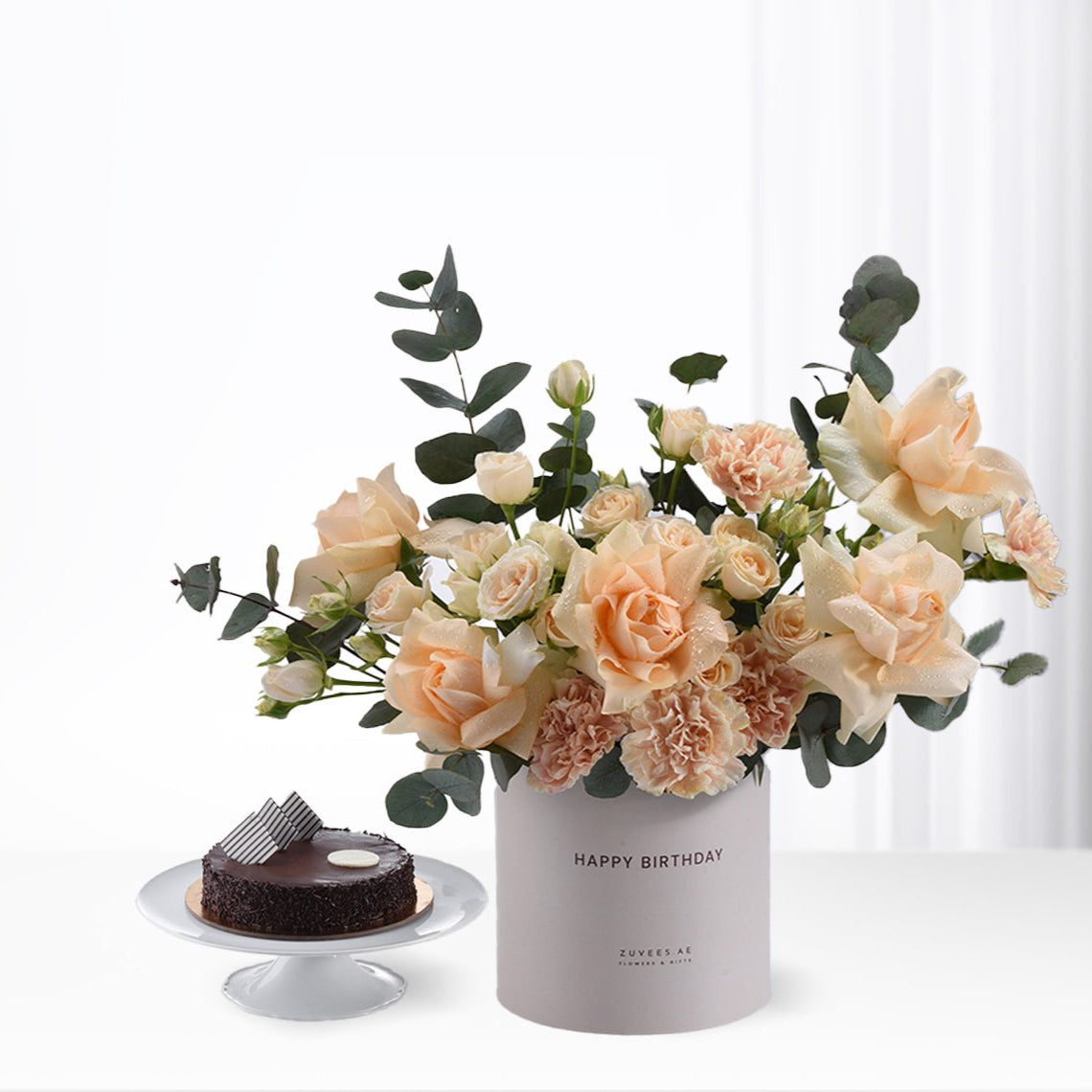 Soft peach roses and eucalyptus in gray "Happy Birthday" vase beside chocolate cake.