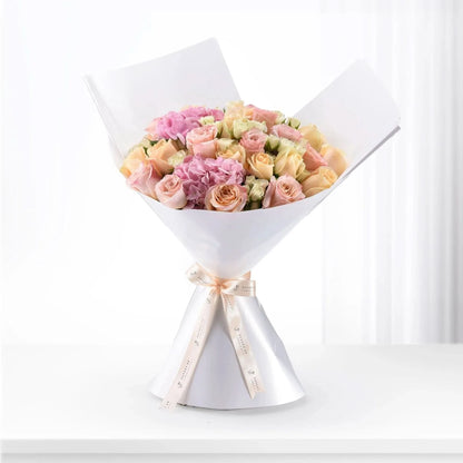 Soft pink and peach roses with hydrangeas, elegantly wrapped in white paper and ribbon.