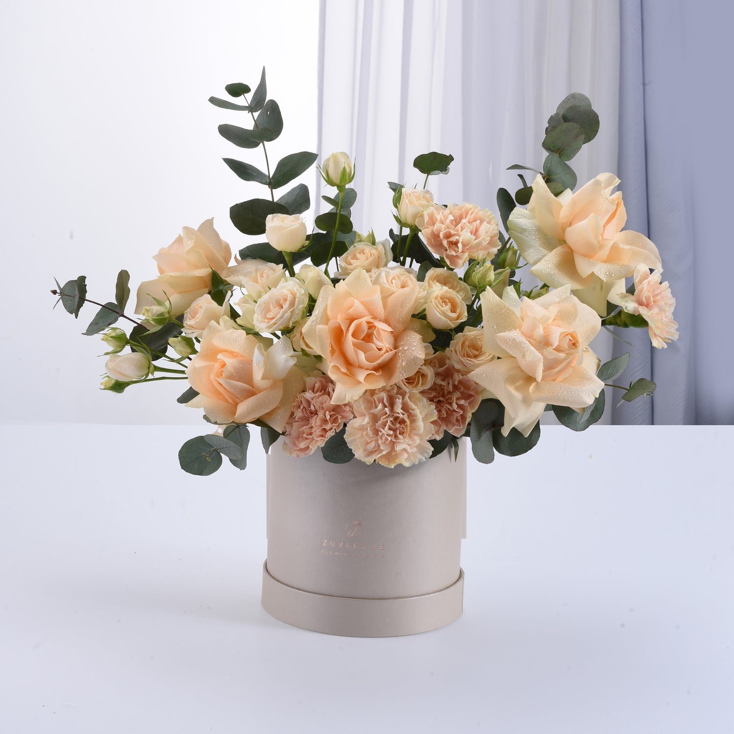 Soft peach roses and carnations in elegant beige hat box with eucalyptus.