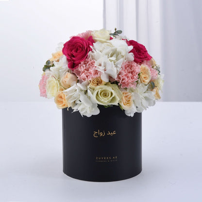 Black box overflowing with vibrant pink, white, and peach roses and hydrangeas.