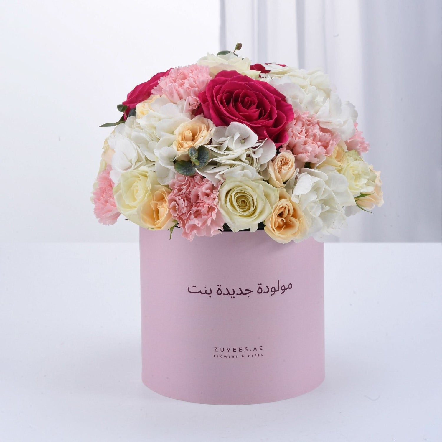 Soft pink box holds vibrant roses, carnations, and hydrangeas for baby girl celebration.