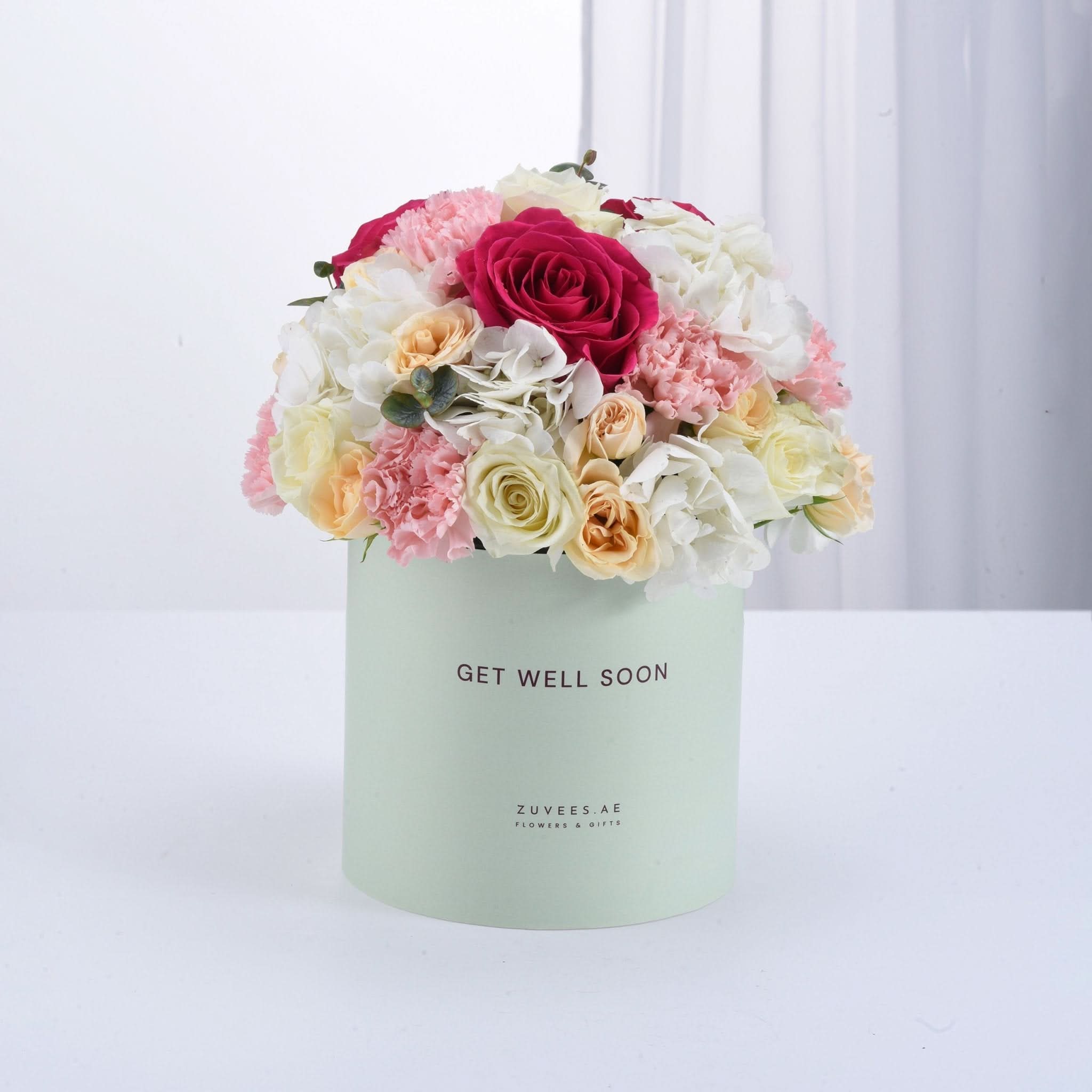 Pastel mint box holds vibrant pink, white, and peach roses and carnations for get-well wishes.