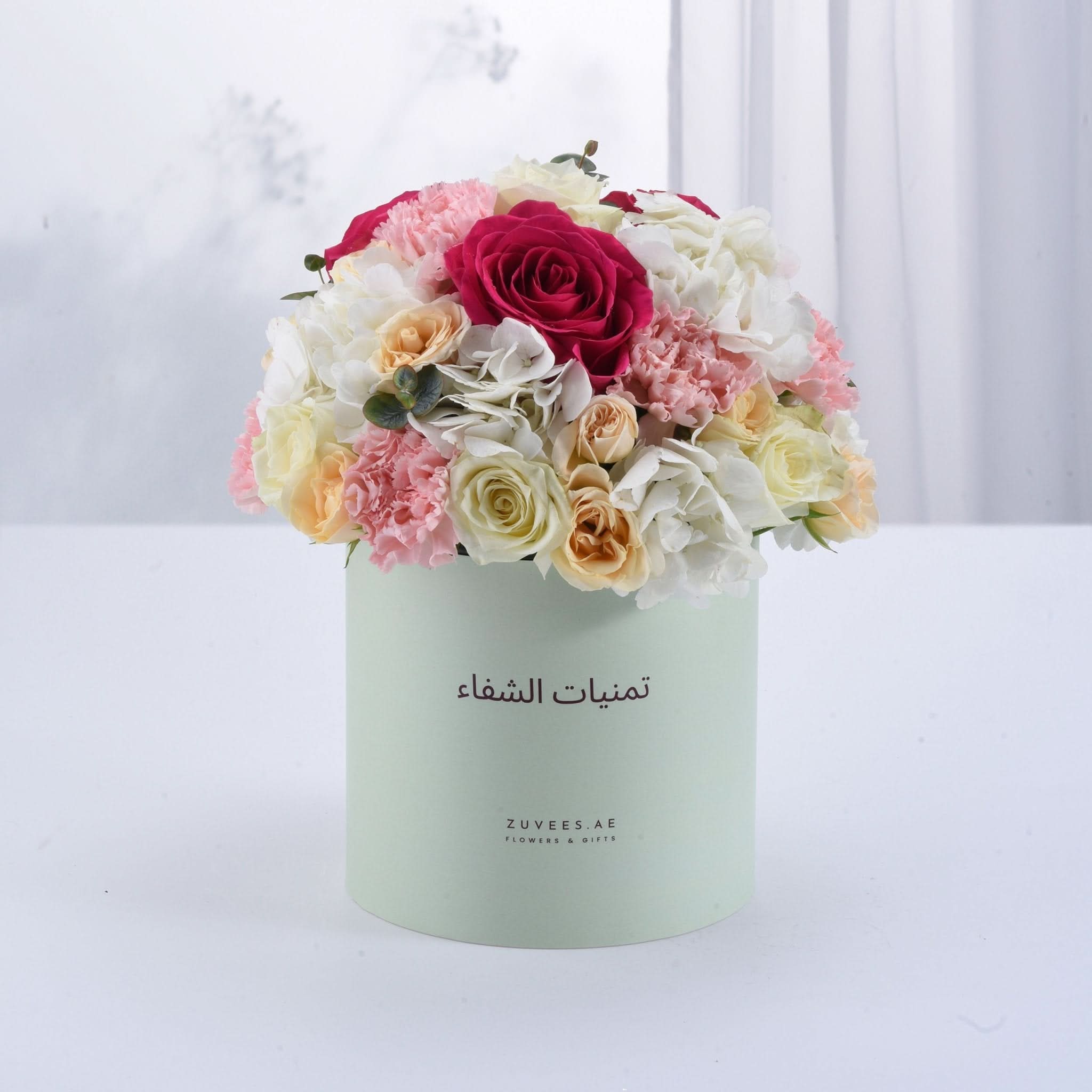Pastel mint box overflowing with vibrant pink, white, and peach roses and hydrangeas.