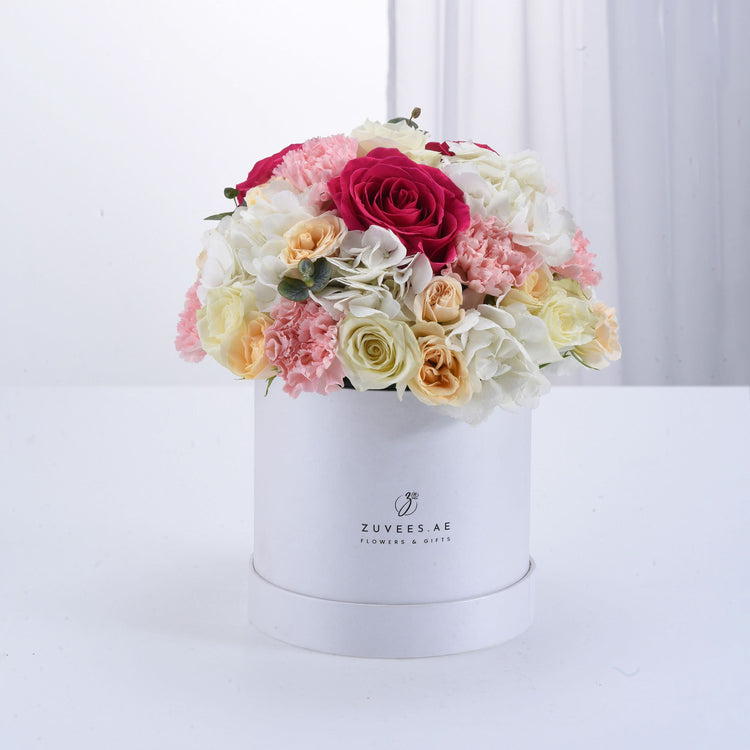 White box overflowing with vibrant pink, cream, and red roses, carnations, and hydrangeas.