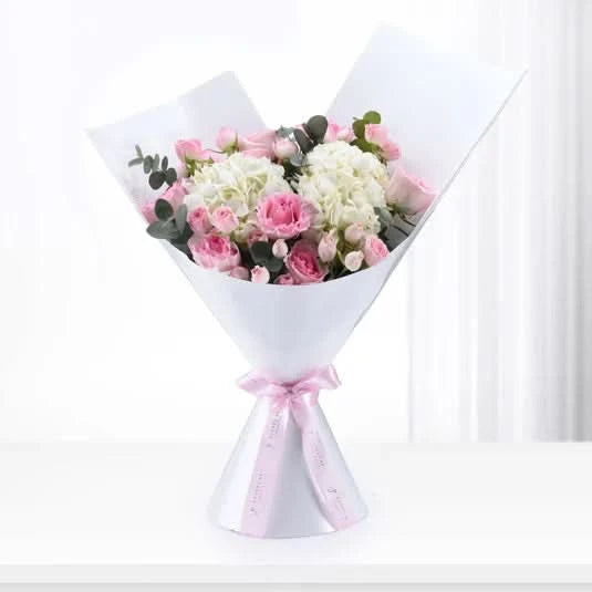 Elegant pink and white rose bouquet wrapped in white paper with pink ribbon bow.