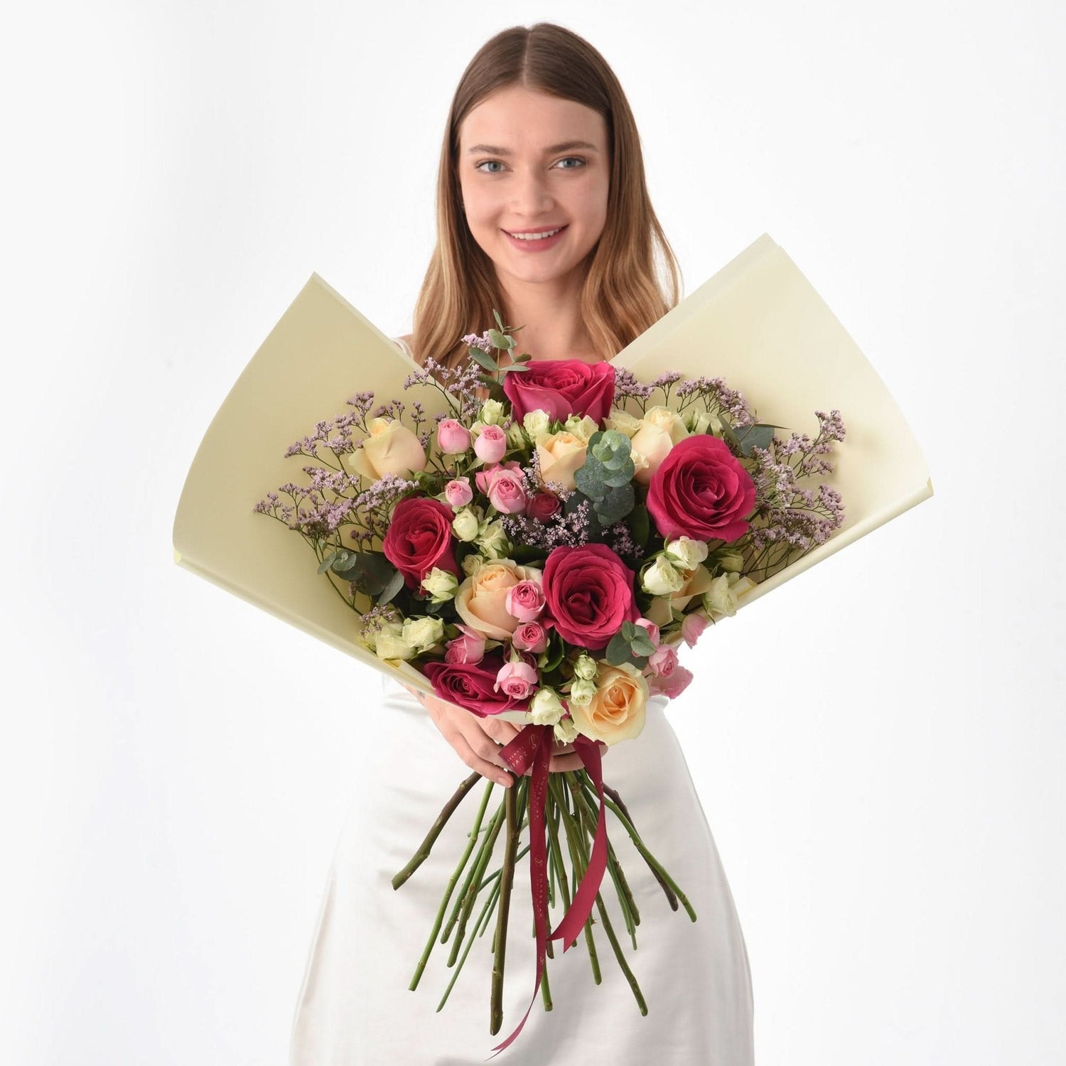 Woman holds vibrant bouquet of pink, red, and cream roses with lavender accents.