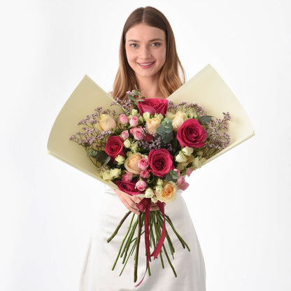 Woman holds vibrant bouquet of pink, red, and cream roses with lavender accents.