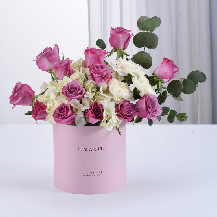 Pink box holds vibrant roses and hydrangeas, celebrating “It’s a Girl” with elegant greenery.