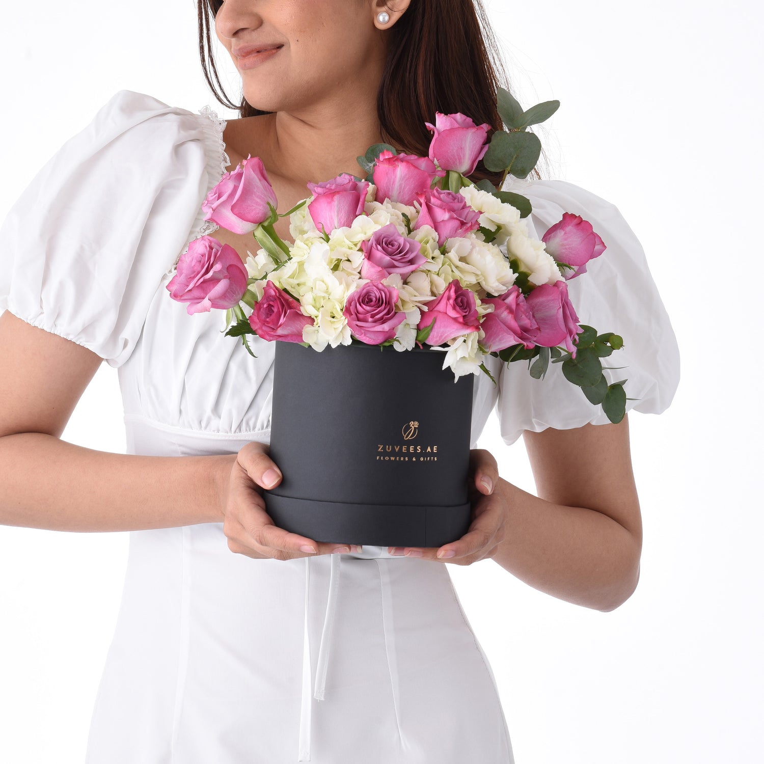 Elegant woman holds black box filled with pink roses and white hydrangeas.