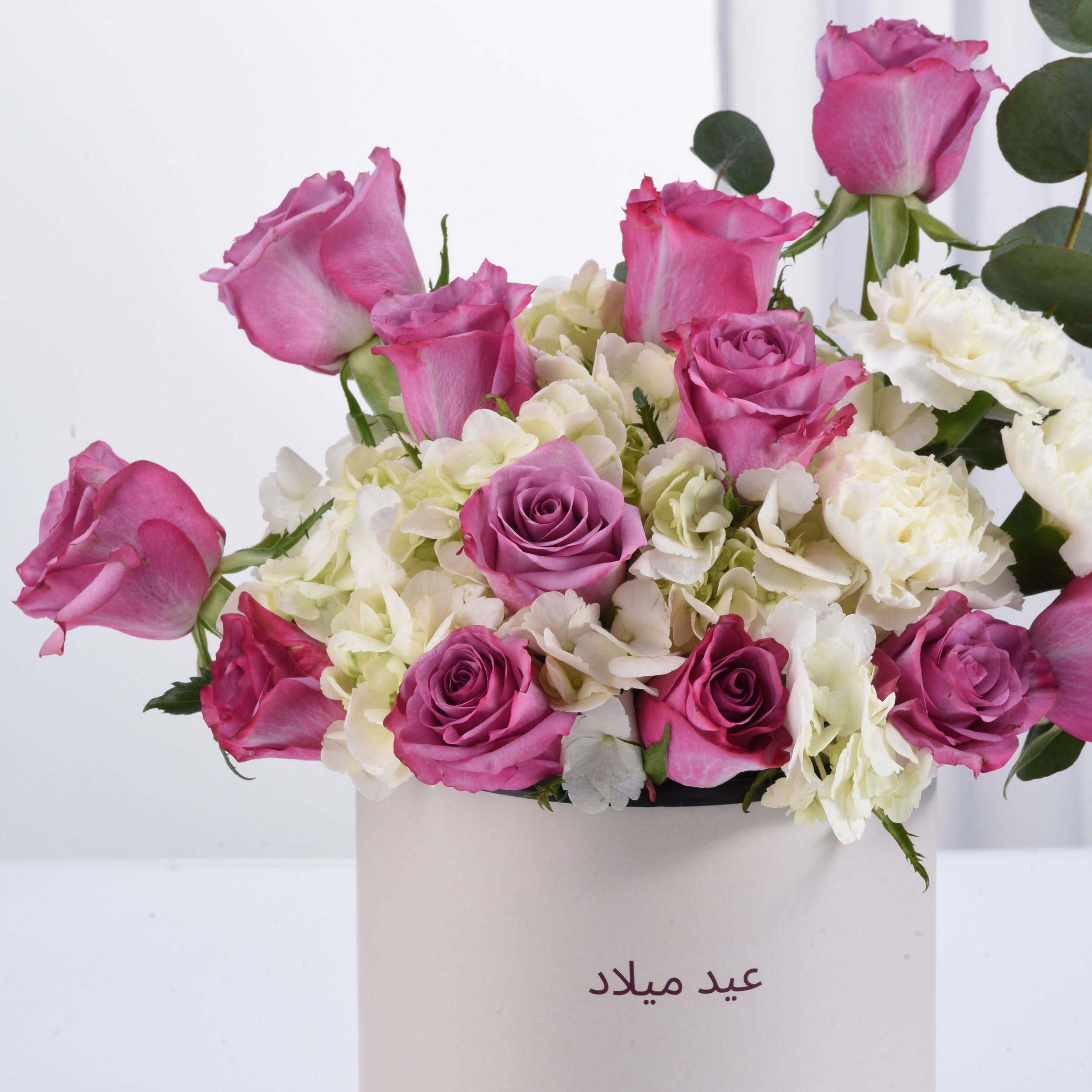 Pink and white roses with hydrangeas in a white box labeled "عيد ميلاد".