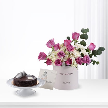 Pink roses, white hydrangeas, eucalyptus in white "Happy Birthday" box beside chocolate cake, greeting card.