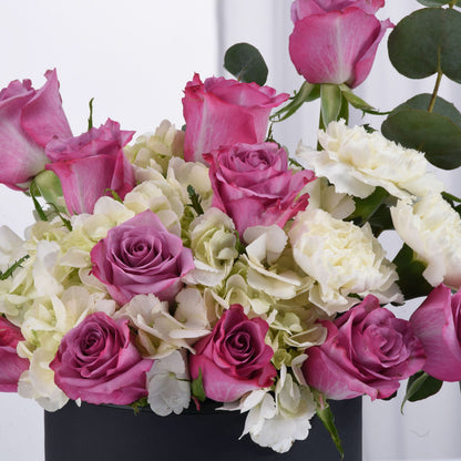 Vibrant pink roses, white hydrangeas, and eucalyptus in sleek black vase.