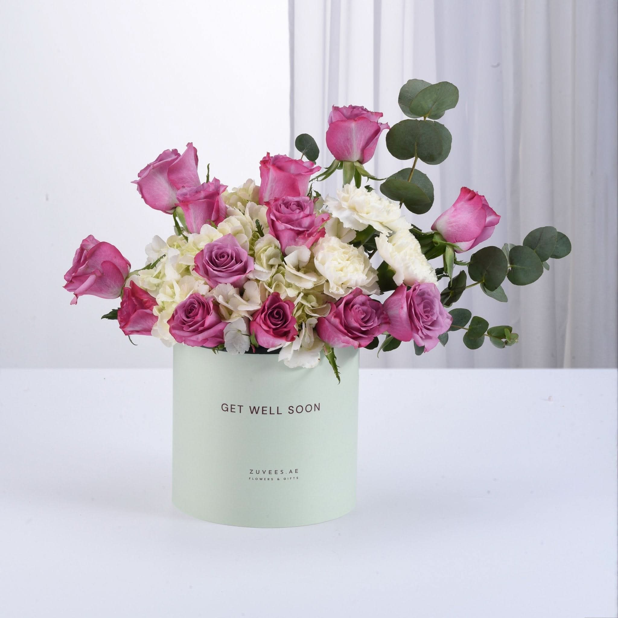 Pastel mint box holds vibrant pink roses, white hydrangeas, and eucalyptus for get-well-soon gift.