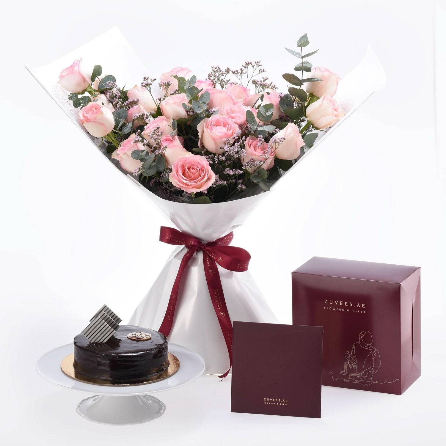 Soft pink roses, chocolate cake, and burgundy gift box elegantly presented.