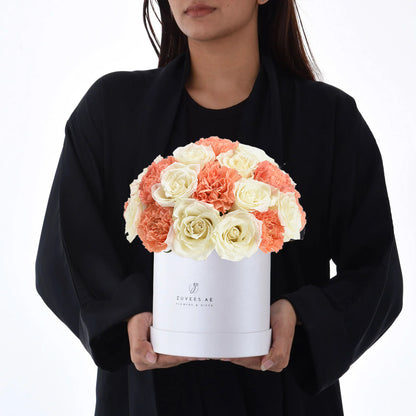 White box holds creamy roses and coral carnations, elegant gift presentation.