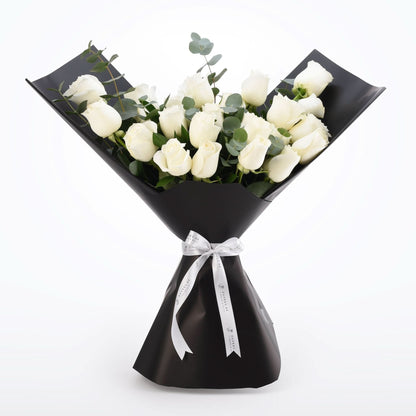 Elegant white roses wrapped in matte black paper with silver ribbon bow.