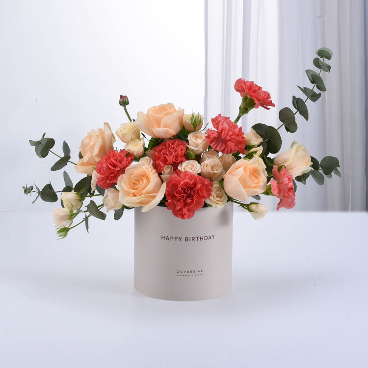 Pastel peach roses and coral carnations in "Happy Birthday" box.