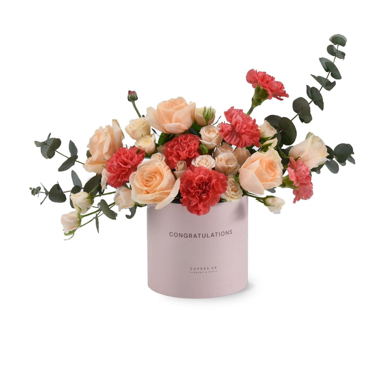 Pink cylinder vase with "CONGRATULATIONS" text, holding peach roses and red carnations with eucalyptus.