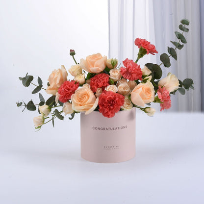Soft pink box holds peach roses and coral carnations, eucalyptus accents.