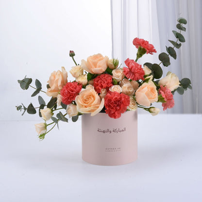 Soft pink box holds peach roses and coral carnations with eucalyptus.