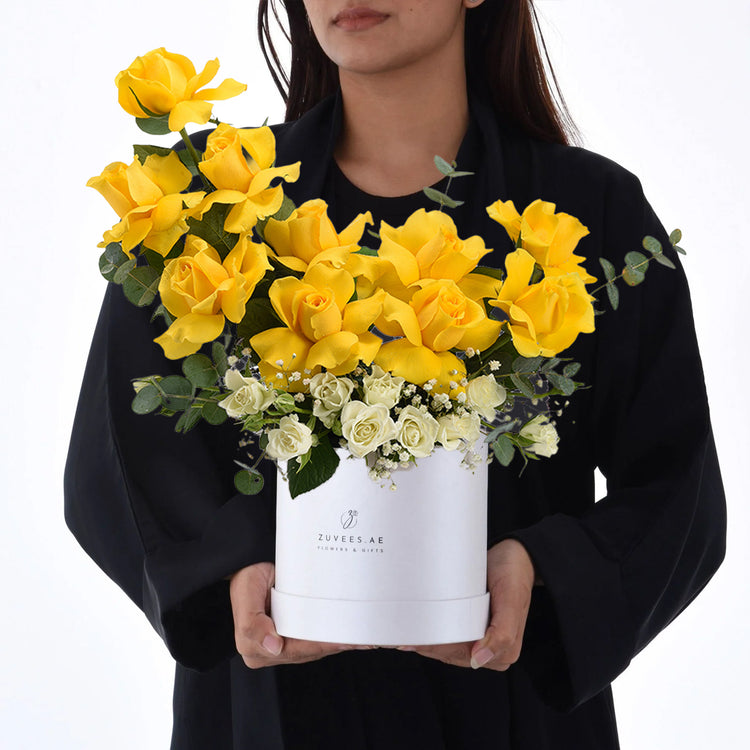 Vibrant yellow roses with white accents in sleek white Zuvees box, held by woman in black.