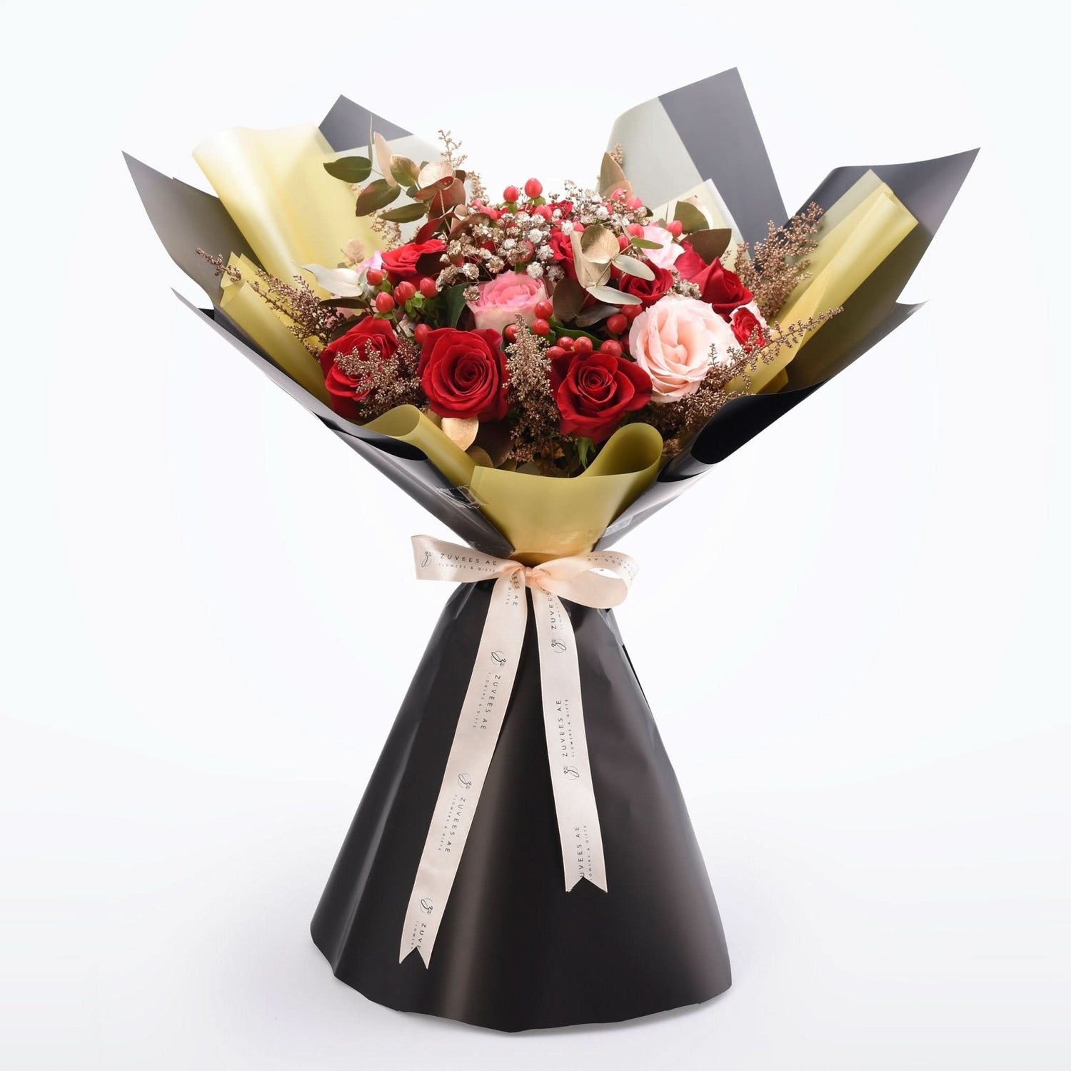Elegant bouquet of red and pink roses, accented with berries and gold foil, wrapped in black and gold paper with branded ribbon.