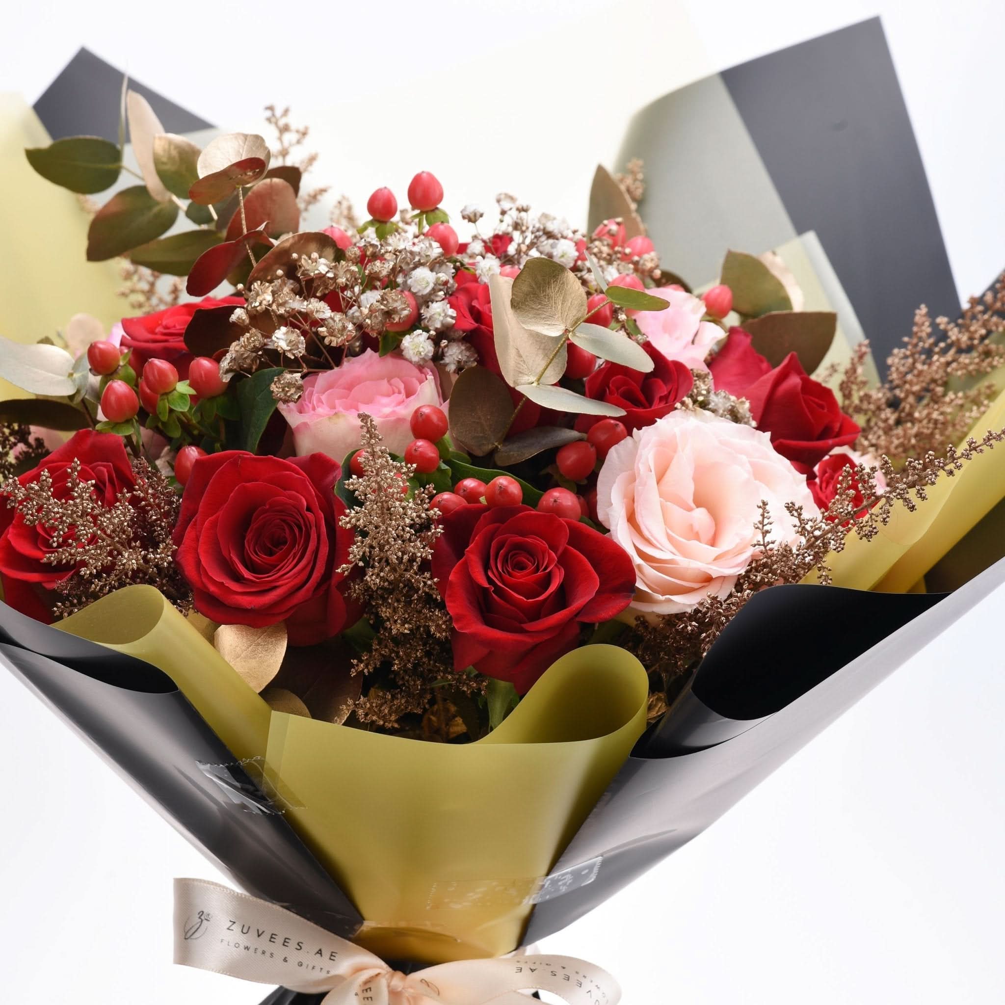 Luxurious bouquet with red and blush roses, berries, and gold accents wrapped elegantly.