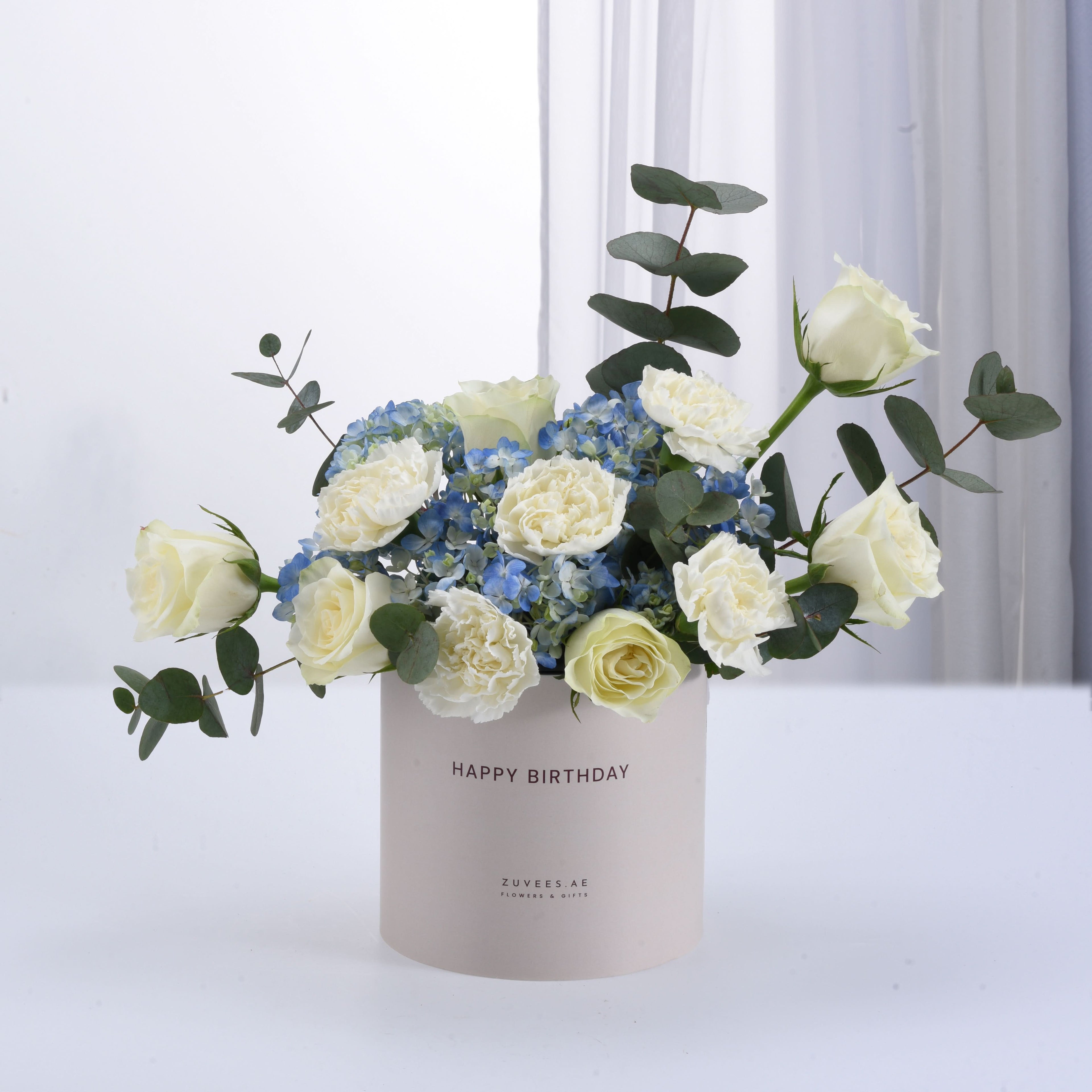 White roses, blue hydrangeas, eucalyptus in "Happy Birthday" vase, elegant gift arrangement.