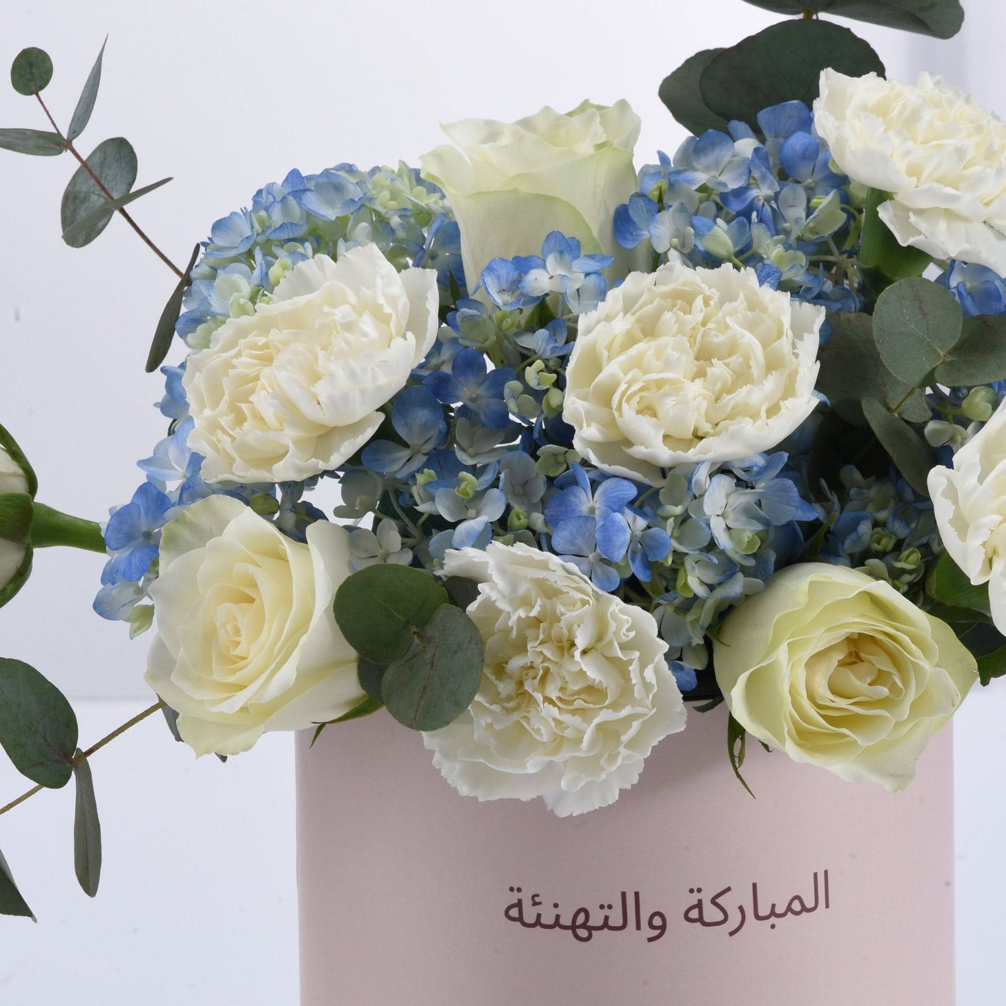 Elegant white roses and blue hydrangeas in pink vase with Arabic "Congratulations" text.