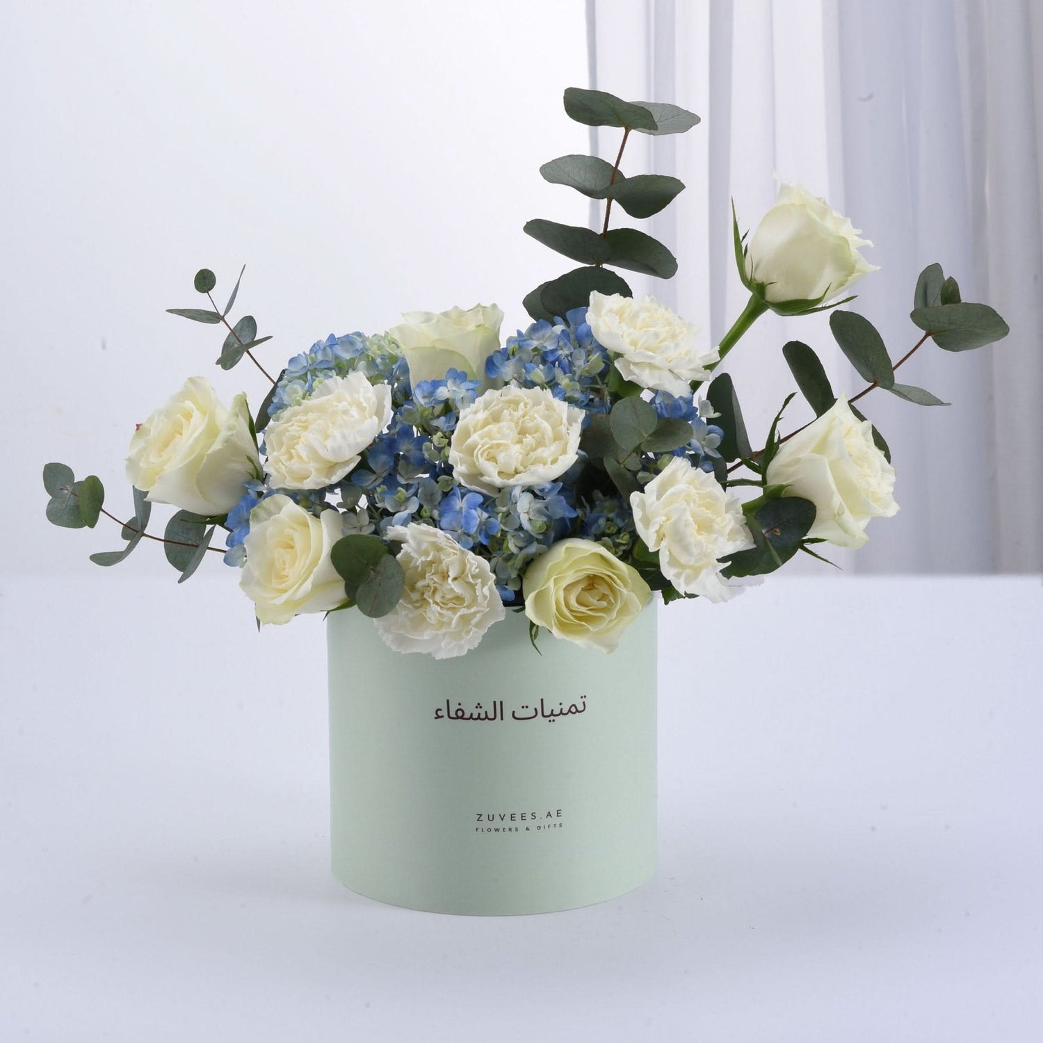 Soft mint box holds creamy white roses, blue hydrangeas, and eucalyptus.