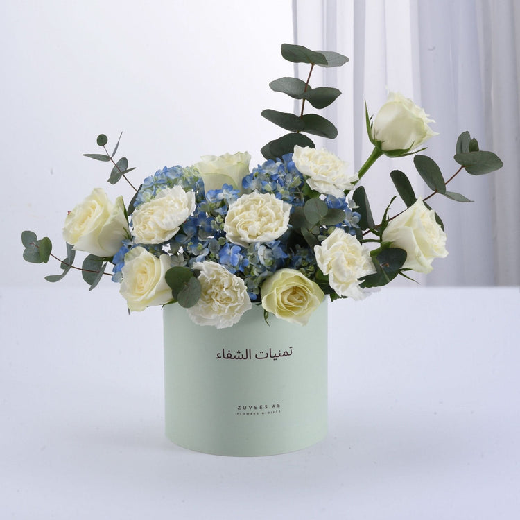 Soft mint box holds creamy white roses, blue hydrangeas, and eucalyptus.