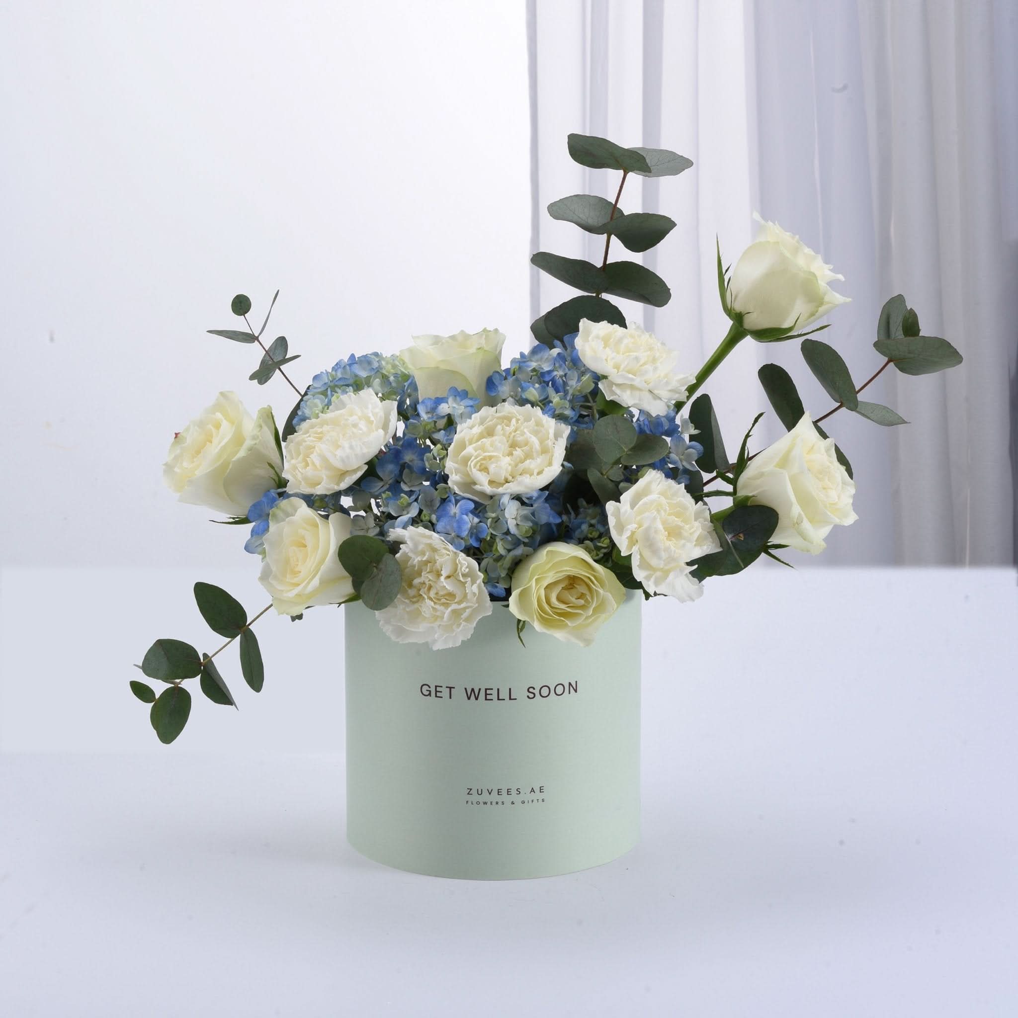 Pastel green box holds white roses and blue hydrangeas, “Get Well Soon” message.