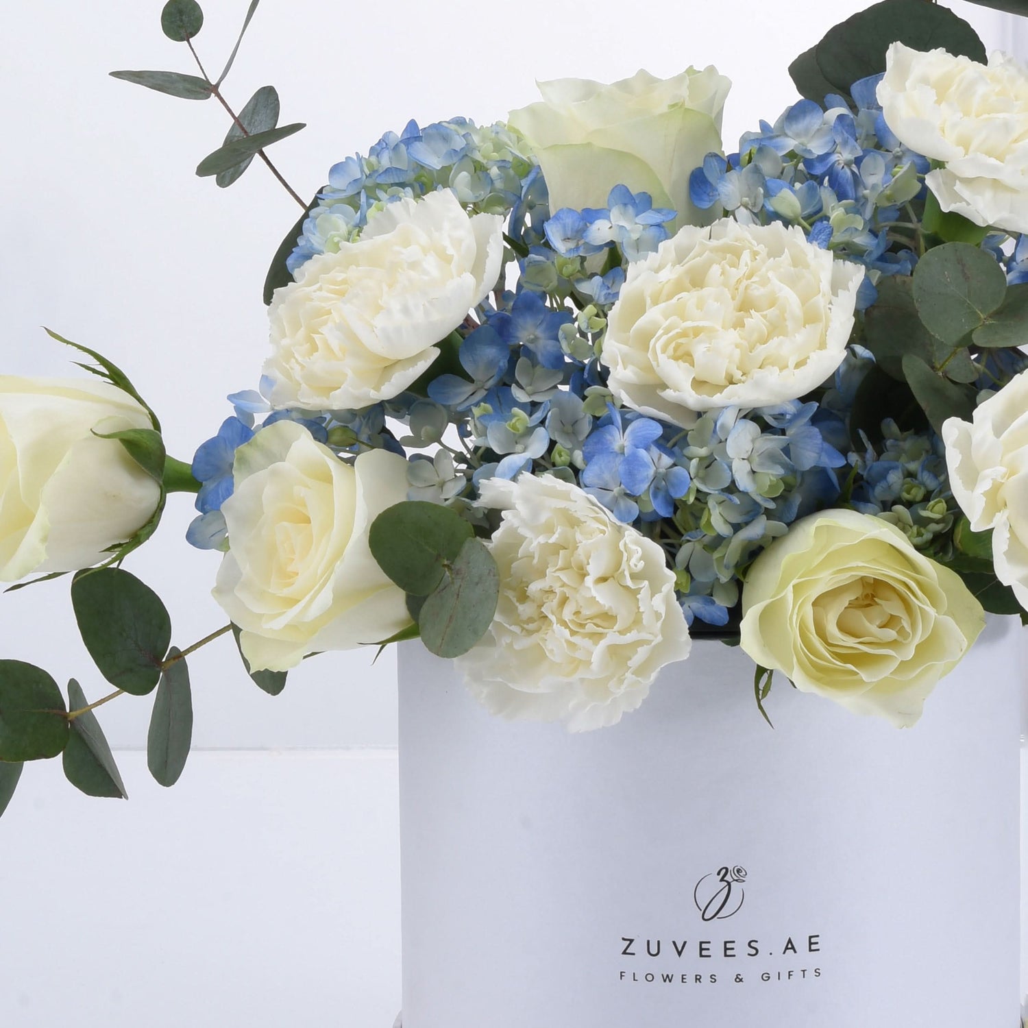 Elegant white roses, peonies, and blue hydrangeas in minimalist white box.