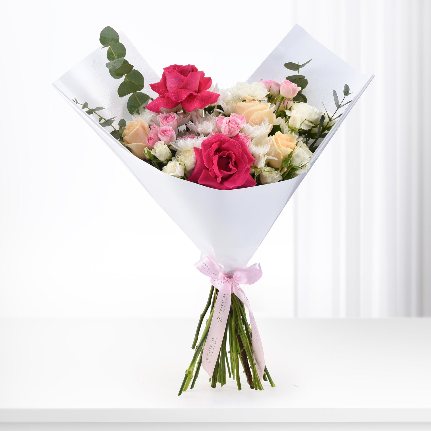 Vibrant pink, white, and peach roses with eucalyptus, wrapped in white paper and pink ribbon.