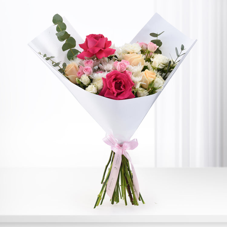 Vibrant pink, white, and peach roses with eucalyptus, wrapped in white paper and pink ribbon.